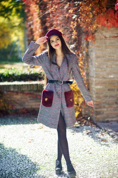 Fiatal szép lány visel téli kabát és sapka őszi levelek háttér. — Stock Fotó