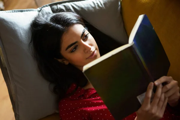 Persian woman at home reading on a couch
