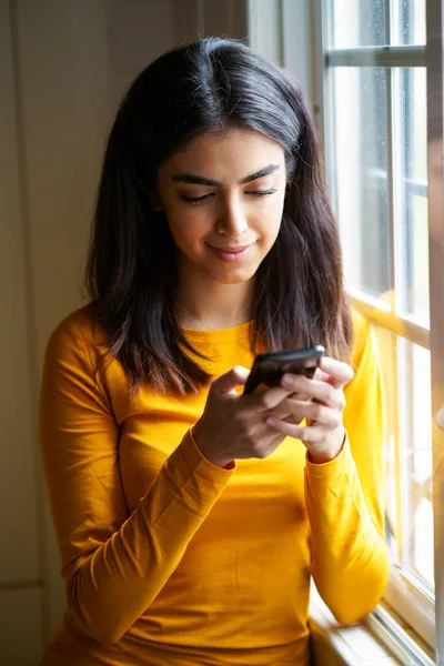 Femme persane utilisant son téléphone intelligent près de la fenêtre — Photo