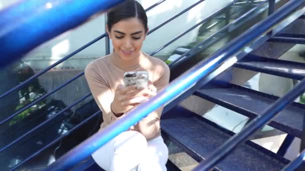 Persian woman using smartphone sitting on urban steps — Stock Video