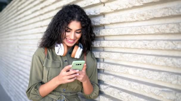 Mujer árabe joven con auriculares usando su teléfono inteligente al aire libre . — Vídeo de stock