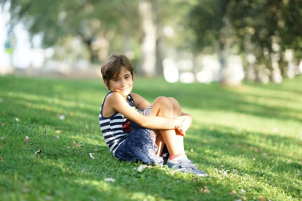 小さな女の子、8歳、屋外の草の上に座って. — ストック写真