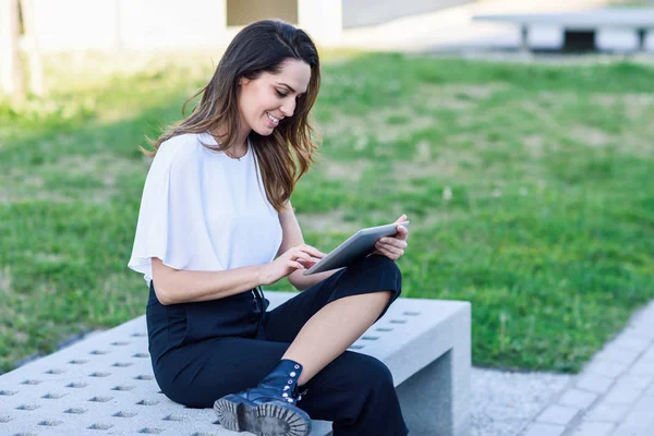 Mujer de mediana edad usando tableta digital sentada al aire libre en el fondo urbano . —  Fotos de Stock