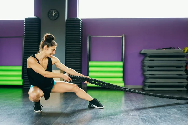 Jonge en atletische vrouw met behulp van trainingstouwen in een fitnessruimte. — Stockfoto