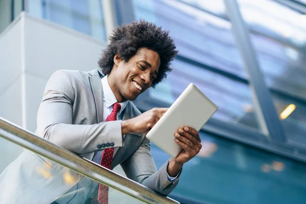 Hombre de negocios negro usando una tableta digital sentada cerca de un edificio de oficinas. — Foto de Stock