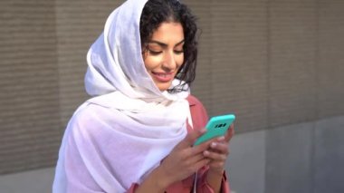 Genç Müslüman kadın tesettürlü akıllı telefonuyla mesaj atıyor..