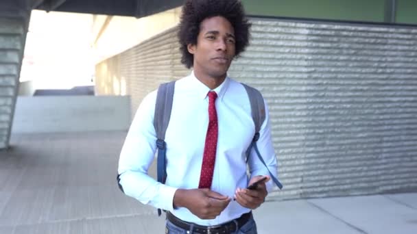 Hombre de negocios negro usando un teléfono inteligente cerca de un edificio de oficinas — Vídeo de stock