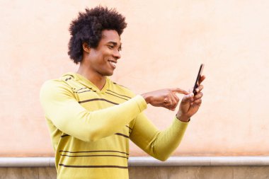 Afro saçlı ve kulaklıklı siyah bir adam akıllı telefon kullanıyor..