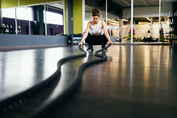 Jeune femme sportive utilisant des cordes d'entraînement dans une salle de gym . — Photo