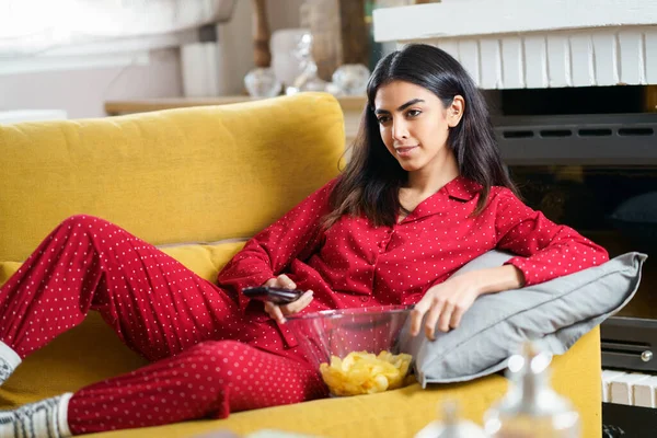 Persian woman at home watching TV and using remote control