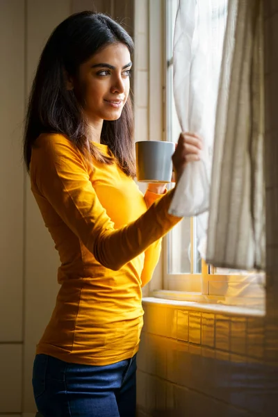 Persian woman drinking coffee while looking through the window