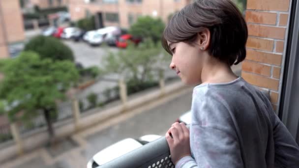 Niña de nueve años mirando por la ventana mientras llueve — Vídeos de Stock