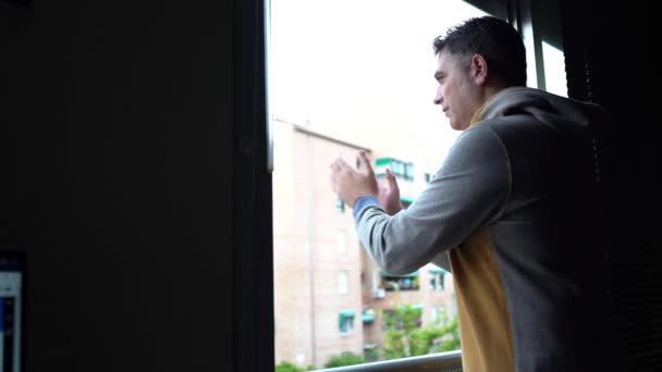 Koronavirüse karşı insanları desteklemek için pencerede alkışlayan bir adam. — Stok video