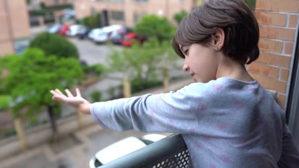 Εννιάχρονο κορίτσι κοιτάζει έξω από το παράθυρο ενώ βρέχει. — Αρχείο Βίντεο
