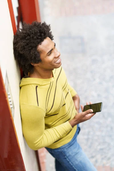 Černoch s afro vlasy a sluchátka pomocí smartphonu. — Stock fotografie