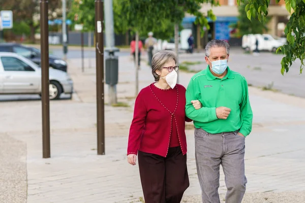 Старшая пара выходит на прогулку в масках, чтобы защитить себя от коронавируса — стоковое фото