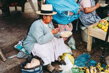 Pisac, Peru - 29 Temmuz 2010: Peru 'daki İndio Market' te Erişte Yiyen Yaşlı Kadın Hasır Şapka Giyiyor.
