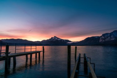 Avustralya 'da bir göldeki iskelede gün doğumu ve dağların manzarası.
