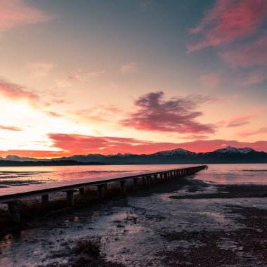 Avustralya 'da bir göldeki iskelede gün doğumu ve dağların manzarası.
