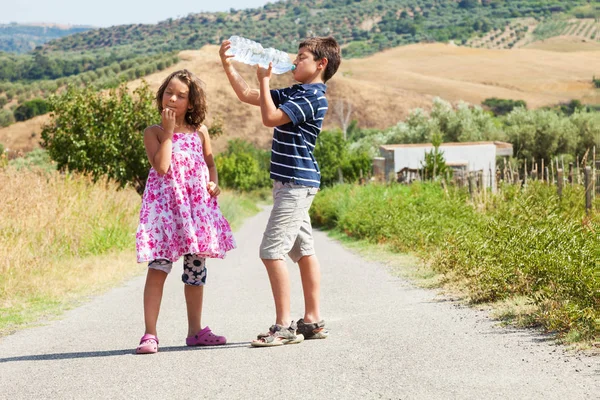 Hermano y hermana en el camino bebiendo agua y pensando en — Foto de Stock