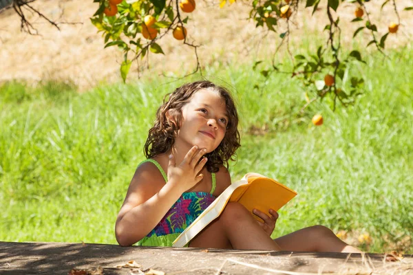 一个美丽的小女孩在花园里读着一本黄色的书 — 图库照片