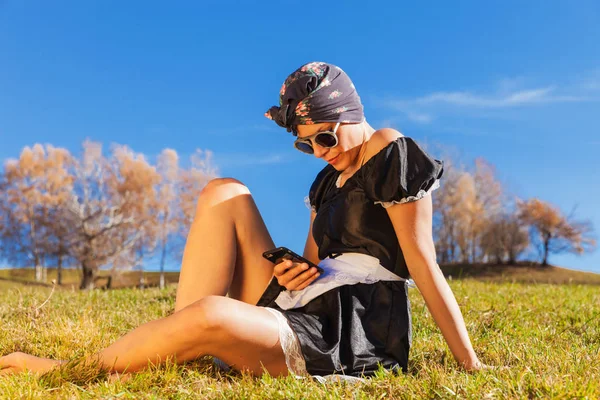 Конец уборщица сидит в траве с телефоном — стоковое фото