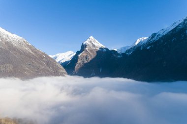 Karlı dağların tepesinde, altında sis var.