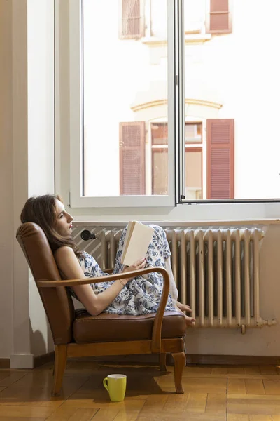 Kvinne Som Sitter Lenestol Nær Vindu Leser Bok – stockfoto