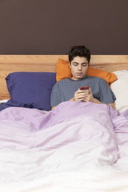 Telefonla yatakta yatan çocuk, sadece zaman kaybediyor ve belki sohbet ediyor ya da bir şeye bakıyor. Ön konum.