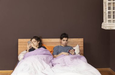 Ağabey ve kız kardeş aynı yatakta telefonla sohbet ediyorlar.