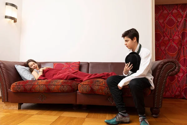 Girl lying on the sofa with a blanket and a young boy is sitting desperately dressed elegantly