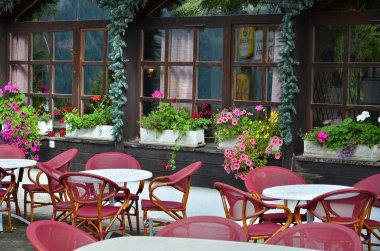 Beyaz yuvarlak masalı, kırmızı sandalyeli ve çiçekli pencereli açık hava restoranı.