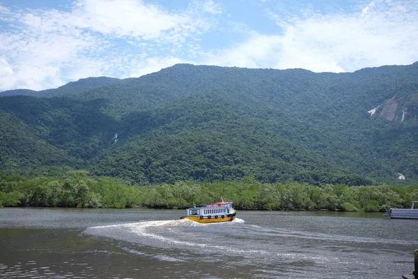 Bertioga Brezilya yakınlarındaki küçük nehri gezen bir yolcu gemisi güneşli bir günde yeşil ormanlı tepelerden önce, vahşi doğa hayatı