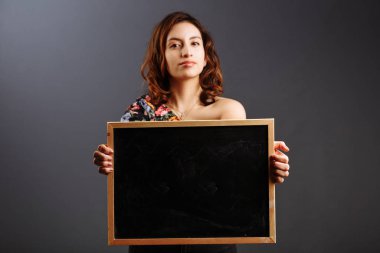 Gri üzerinde izole edilmiş boş bir karatahta tutan Latin Amerikalı genç kız öğrencinin portresi