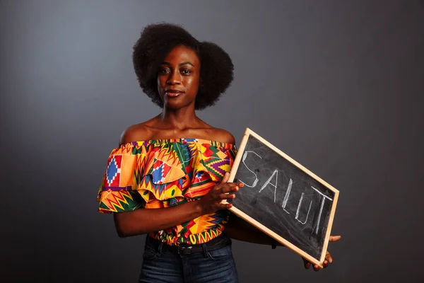 Portrét mladé africké studentky v šatech drží tabuli s ahoj slovo v jejím rodném jazyce izolované na šedém pozadí — Stock fotografie