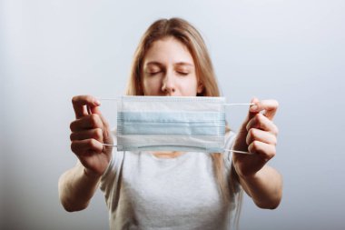 Genç ve güzel bir kadın Coronavirus bulaşıcı hastalığına karşı tıbbi maske takıyor. hafif bir arka planda. Sıhhiye maskesini tutuyor. Koronavirüs COVID-19 'a karşı önleyici önlem.