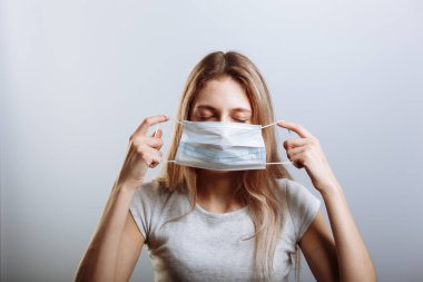 Genç ve güzel bir kadın Coronavirus bulaşıcı hastalığına karşı tıbbi maske takıyor. hafif bir arka planda. Sıhhiye maskesini tutuyor. Koronavirüs COVID-19 'a karşı önleyici önlem.