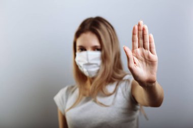 Yüz maskeli kadın virüslerin yayılmasını önlemek için dur işaretini eliyle gösteriyor. Seçici odak.