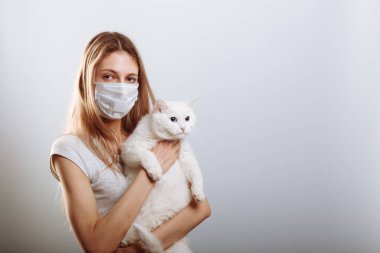 Koruyucu cerrahi maske takan kadın kedi yüzlü bir maske takıyor. Çin Coronavirüs Hastalığı COVID-19 evcil hayvanlar için tehlikelidir.