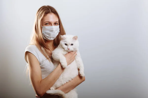 Woman in protective surgical mask holds cat pet in face mask. Chinese Coronavirus disease COVID-19 is dangerous for pets.