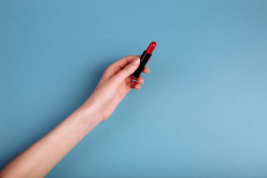 Kadının eli kırmızı ruj alıyor. Mavi arkaplanda izole edilmiş.