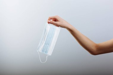 Bir kadın eli, beyaz arka planda izole edilmiş tıbbi bir maske tutuyor..