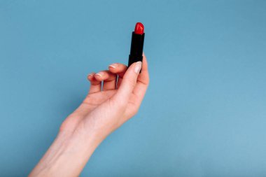 Kadının eli kırmızı ruj alıyor. Mavi arkaplanda izole edilmiş.