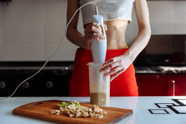 Woman with hand blender making sweet banana protein powder milkshake smoothie. protein shake after workout. sport nutrition diet after gym. Healthy lifestyle.