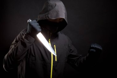 Bilinmeyen, siyah elbiseli, bıçaklı bir haydut kurbana bıçakla saldırıyor. Konsept: 19. kriz nedeniyle suç. Siyah arka planda izole edilmiş. Seçici odak.