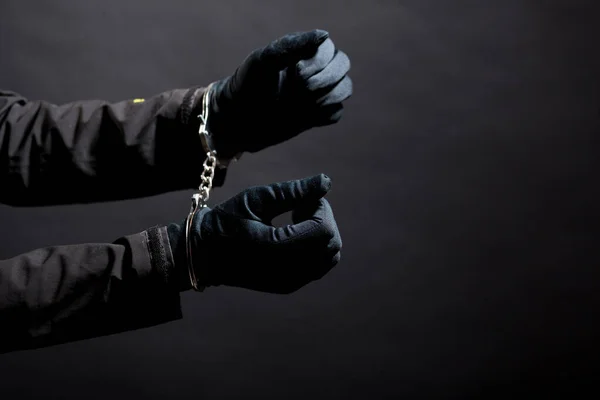 Siyah eldivenli, siyah arka planda kelepçeli bir hırsızın elleri..