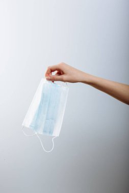 Bir kadın eli, beyaz arka planda izole edilmiş tıbbi bir maske tutuyor..