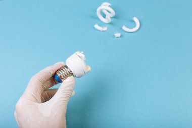 Bir adam elinde eldivenle mavi arka planda kırık bir floresan spiral lamba ile enerji tasarrufu lambası tutuyor. Dikkat, zehirli gaz..
