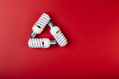 Mavi üzerine izole edilmiş geri dönüşüm işareti şeklinde üç enerji tasarrufu lambası. Kırmızı arkaplan üzerindeki metin için başlık.