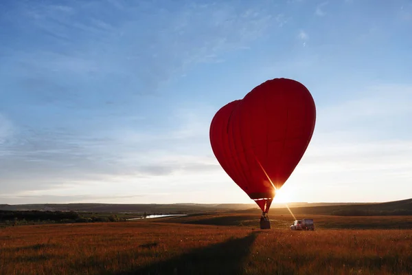 Hot Red air balloon heart shape flying into sunset over valley landing or taking off — Stock Photo, Image